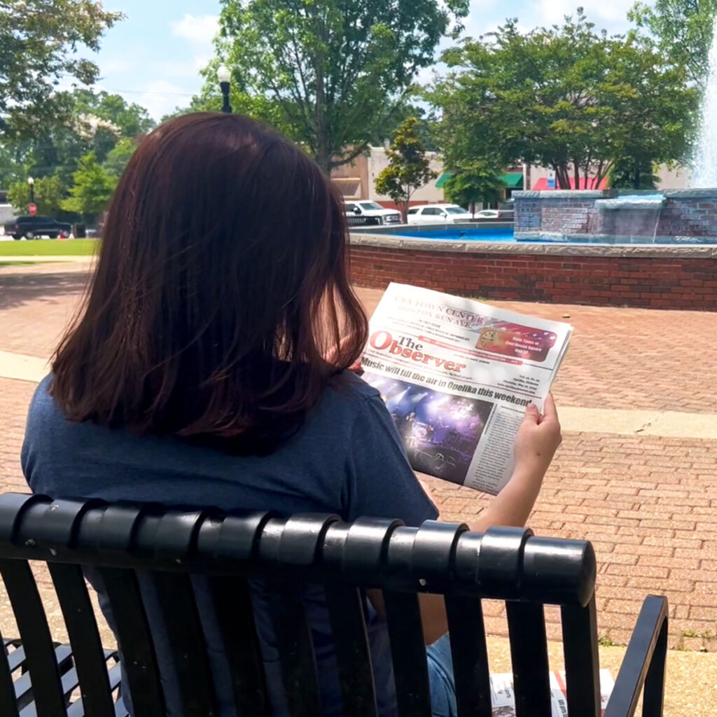 A woman reading the observer on a bench near the Opleika courthouse.